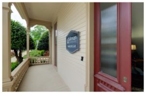 Front porch of Raleigh divorce law firm - Charles R. Ullman & Associates. Tan siding with red door with a window, and a plaque with the firm name. 